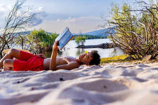Young man relaxing on beach reading book enjoying the summer vacation by lake