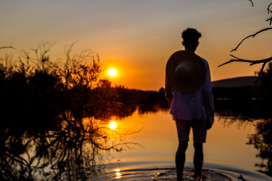 Person standing in water watching summer sunset over lake with reflections