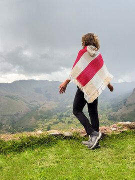 Woman wearing poncho standing and enjoying views of Andes mountains in Peru