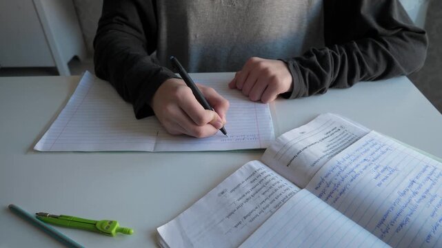 Writing with pen on quiet study space. Bright natural light illuminates student notes. Focused student practices writing with pen in peaceful environment
