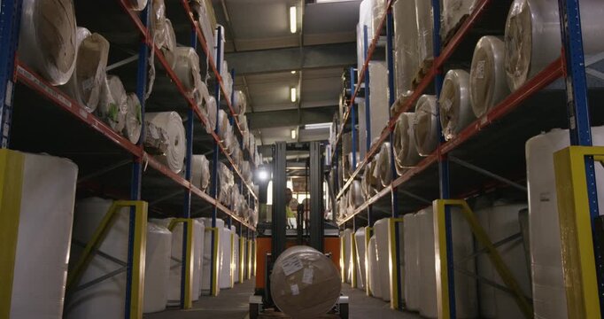 Forklift moving a pallet with a large roll through a warehouse aisle