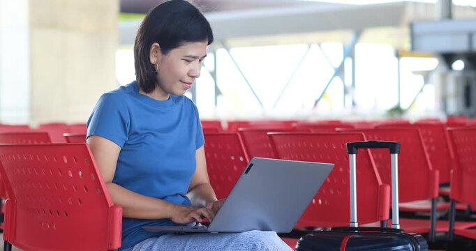Young Asian woman using a laptop while waiting with luggage, remote work, digital nomad lifestyle, travel, productivity, and modern mobility, Thai people