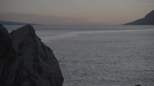 Peaceful Adriatic Sea at dusk in Brela, Croatia, featuring a rocky coastline, calm blue water and a tranquil Mediterranean evening landscape