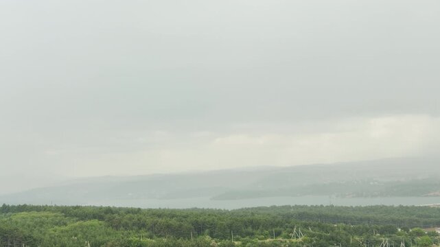 A gentle summer shower falls over the quiet reservoir and forests of Simferopol, Crimea. The misty landscape evokes a peaceful, melancholic feeling.