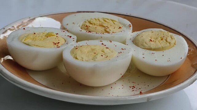 Close up of chili pepper powder spice flakes falling on boiled eggs served inside plate. Hardboiled and half sliced egg adding seasoning or garnish with flavouring dust. Simple protein diet snack.