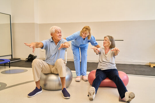 Seniors practicing rehabilitation exercises with assistance on stability balls in rehab facility