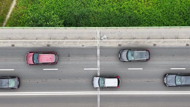 Aerial view of a traffic jam on a busy road, showcasing multiple vehicles including cars and a bus, surrounded by greenery and urban infrastructure in a vibrant setting