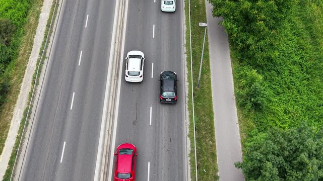 Aerial view of a traffic jam on a busy road, showcasing multiple vehicles including cars and a bus, surrounded by greenery and urban infrastructure in a vibrant setting