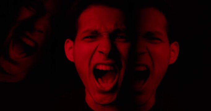 Man screaming in dramatic red lighting. Portrait of angry duality person, intense aggression, mental health disorder. Concept of fear, hysteria, instability, split mind. Two personality inner struggle