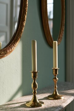 Brass candlesticks on travertine shelf beneath vintage mirrors in Scandinavian interior