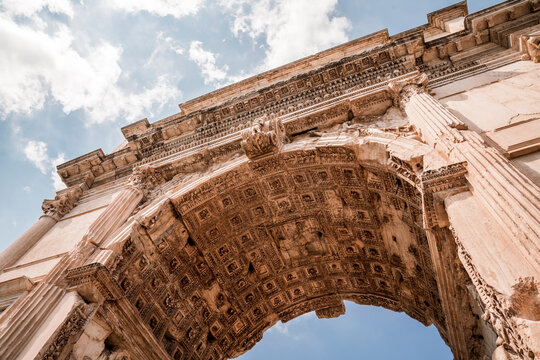 Low angle view of a carved ancient Roman triumphal arch with coffered ceiling, columns and ornamental reliefs