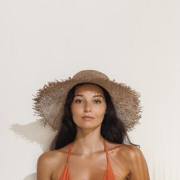 Tanned Woman In Straw Hat And Bikini Posing Against Minimalist Backdrop