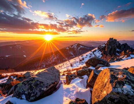 Majestic mountain range at sunset with golden sunbeams illuminating snow-capped peaks.