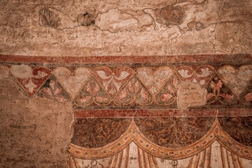 Faded ancient fresco mural with decorative frieze and scalloped arch motifs on weathered plaster wall in historic interior © PIC by Femke