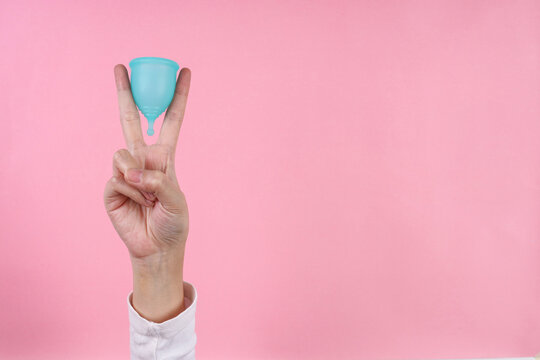 Adult Female Hand Makes Peace Sign While Holding Silicone Menstrual Cup Isolated On Pink Background