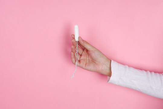 Woman Hand Reaches From The Right Holding Tampon Upright Against Pink Background