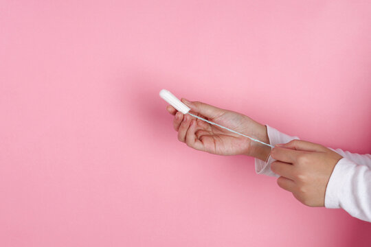 Adult Female Two Hands Pulling The String Of Cotton Tampon Against Pink Background