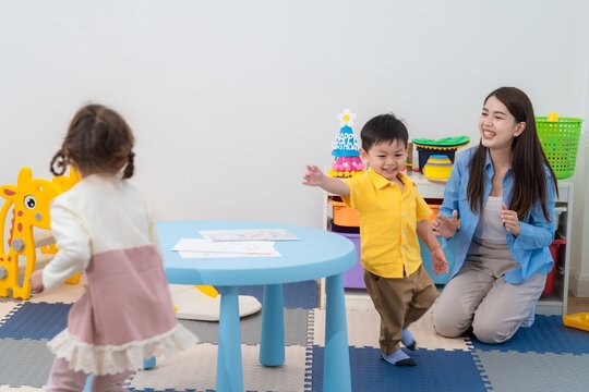 Children play in a colorful room while a teacher watches and encourages them during an activity
