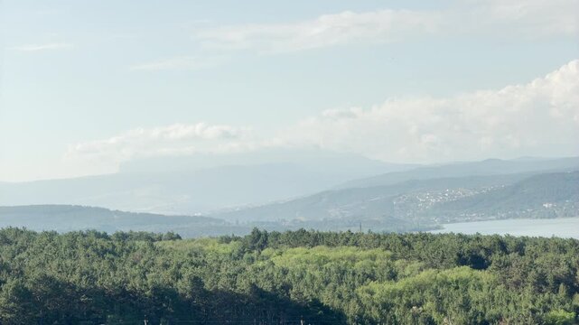 Mount Chatyr-Dag rises quietly behind misty clouds over a lush green forest and reservoir in Simferopol, Crimea. This vast, bright landscape creates a deeply peaceful and serene feeling.