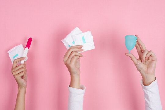 Three Hands Hold Pregnancy Test Sanitary Pads And Menstrual Cup Isolated On Pink Background