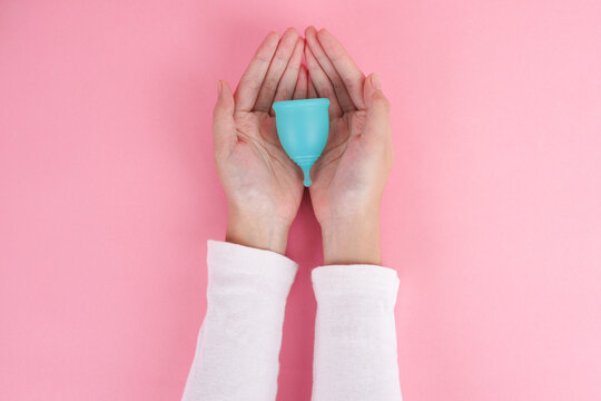 Cupped Hands Reach Upward Holding Reusable Silicone Menstrual Cup Against Solid Background