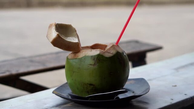 Fresh young coconut ready to drink, served with a red straw.	