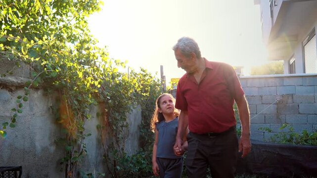 An elderly man and young girl walk hand in hand in a green garden, sharing a warm family moment of trust, affection, childhood, nature, intergenerational bond and peaceful rural life.