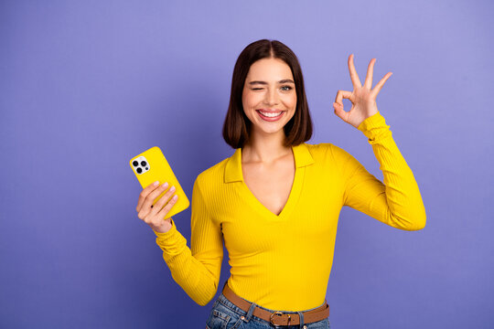 Young chic student smiles and poses with yellow phone against purple background showcasing fashion style and modern lifestyle