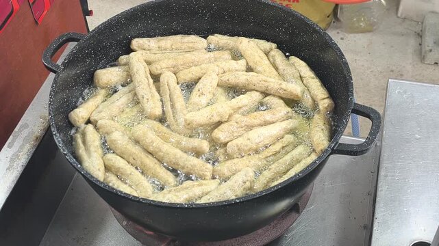 Sizzling keropok lekor being deep-fried to perfection in hot oil. This traditional Malaysian fish cracker snack from Terengganu is made from a flavorful blend of fish paste and flour.