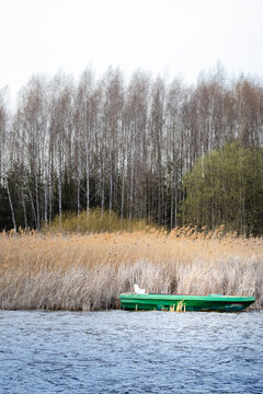 Abandoned wooden boat resting near reeds on calm lakeshore in soft spring light. Atmospheric natural scene with rustic textures. Solitude, time passing and quiet reflection in Siemianowka, Poland.