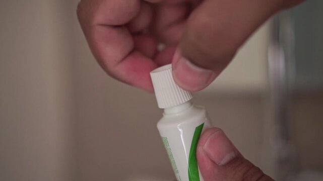 hands closing a toothpaste cap in a bathroom. Personal hygiene routine, dental care preparation, and oral health concept with everyday grooming activity.