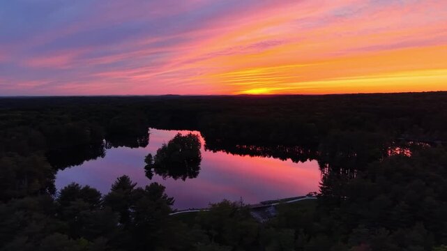 Stunning aerial view of pink and orange sunset reflecting on a tranquil lake at Harold Parker State Forest, Andover, Massachusetts