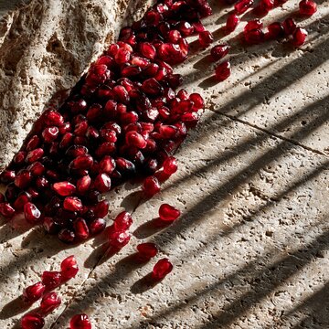Vibrant Red Pomegranate Arils on Textured Stone with Sunlight Shadows