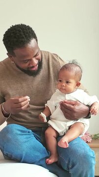 A man sits with a baby on his lap, gently engaging the child in a cozy home setting.