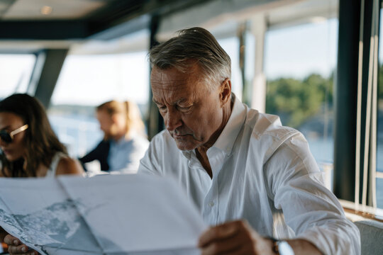 A distinguished older man perusing a map, capturing the essence of adventure and exploration in a comfortably stylish yacht environment, surrounded by serene water views.