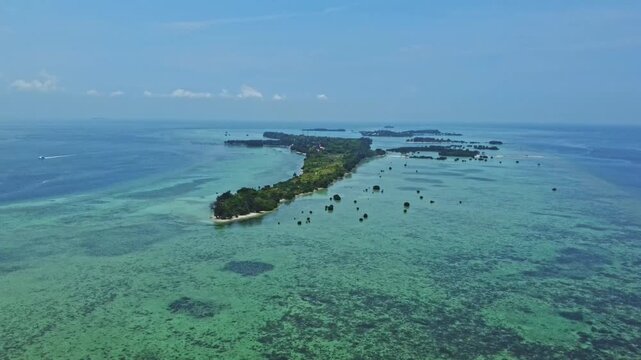 Aerial view of a tropical island archipelago surrounded by clear turquoise sea and coral reefs. Drone shot of an island strip with green trees in the ocean. Pari island in Indonesia 