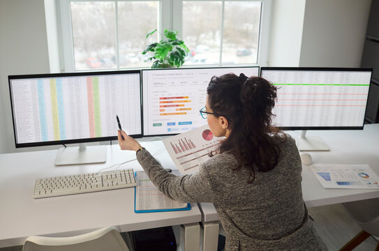 Analyst woman reviews data report charts on monitors. In a bright office she conducts analysis, comparing spreadsheets and dashboards on a computer. Clear business performance tracking concept.