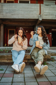 Young women friends eating take out noodles outdoors