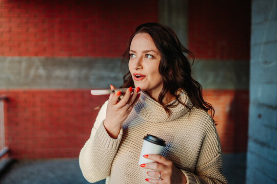 Woman recording voice message on phone holding coffee