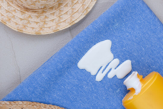 Close-up of white sunscreen lotion spilled from a yellow bottle onto blue fabric with summer accessories nearby. Concept cosmetic stains on the cloth. top view