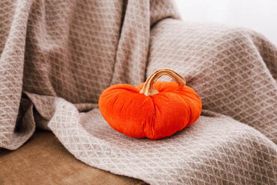 Bright orange pumpkin sits on a soft blanket in a cozy indoor setting during the autumn season