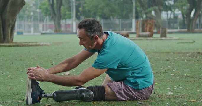 Adult with a lower limb prosthesis completing a seated flexibility exercise in a public park, illustrating adaptive rehabilitation, physical conditioning, mobility improvement, resilience, self care, 