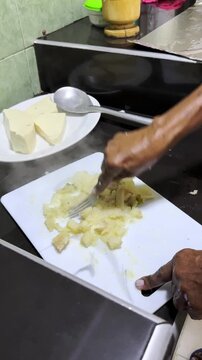 Cook mashing steaming hot cassava on cutting board