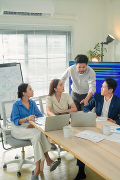 Serious business team analyzing data on laptops and dashboard screen in meeting room, colleagues discussing strategy with charts and documents, focused corporate decision making scene
