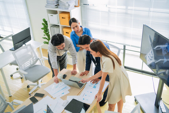 Focused business team analyzing data on laptop screen in office, colleagues reviewing charts and reports together, serious workplace collaboration and problem solving, professional teamwork moment
