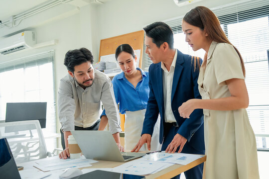 Focused business team analyzing data on laptop screen in office, colleagues reviewing charts and reports together, serious workplace collaboration and problem solving, professional teamwork moment
