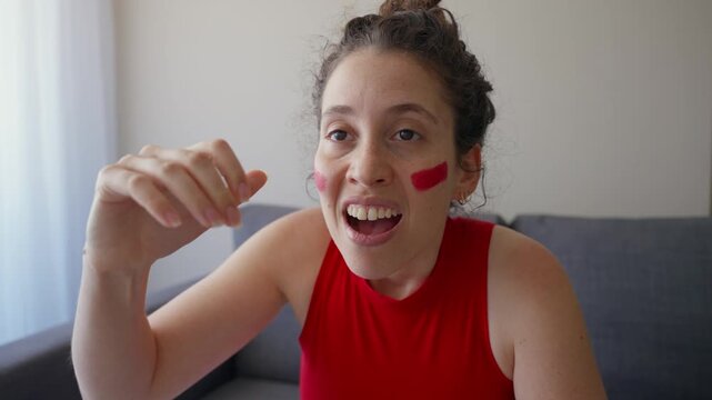Excited fan watching game on TV is disappointed by result or loss of favorite team. Passionate supporter dressed in red with face paint in living room is upset and sad by defeat or miss in sport match
