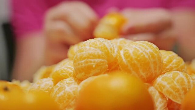 Macro view of juicy mandarin pieces with man peeling citrus in soft focus