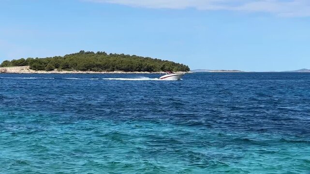 Boat speeds across blue water near an island in a clear sky during day time in Croatia