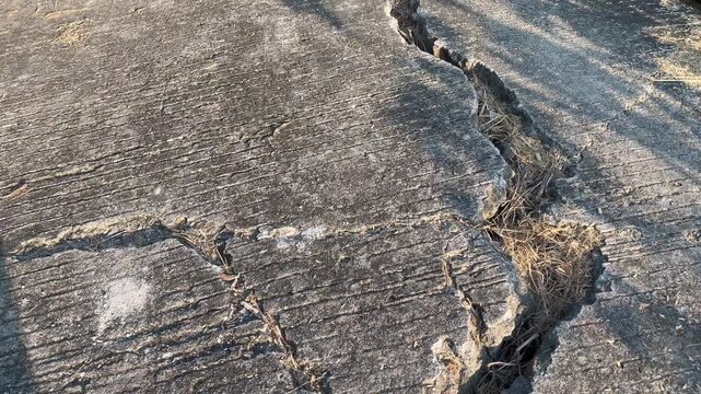 Deep crack on combed concrete road with weeds growing